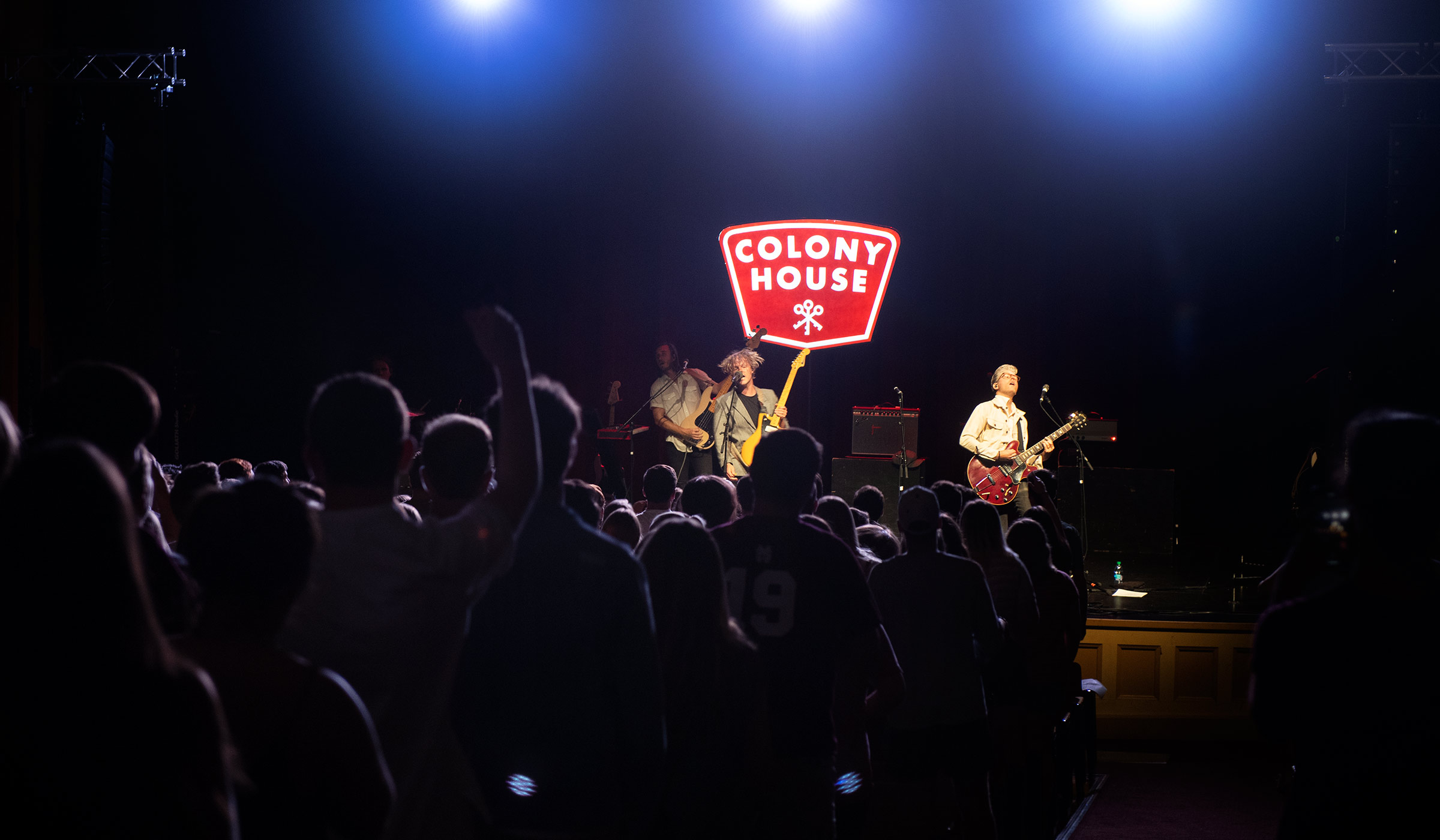 Crowd in foreground to the left and band on stage playing guitars