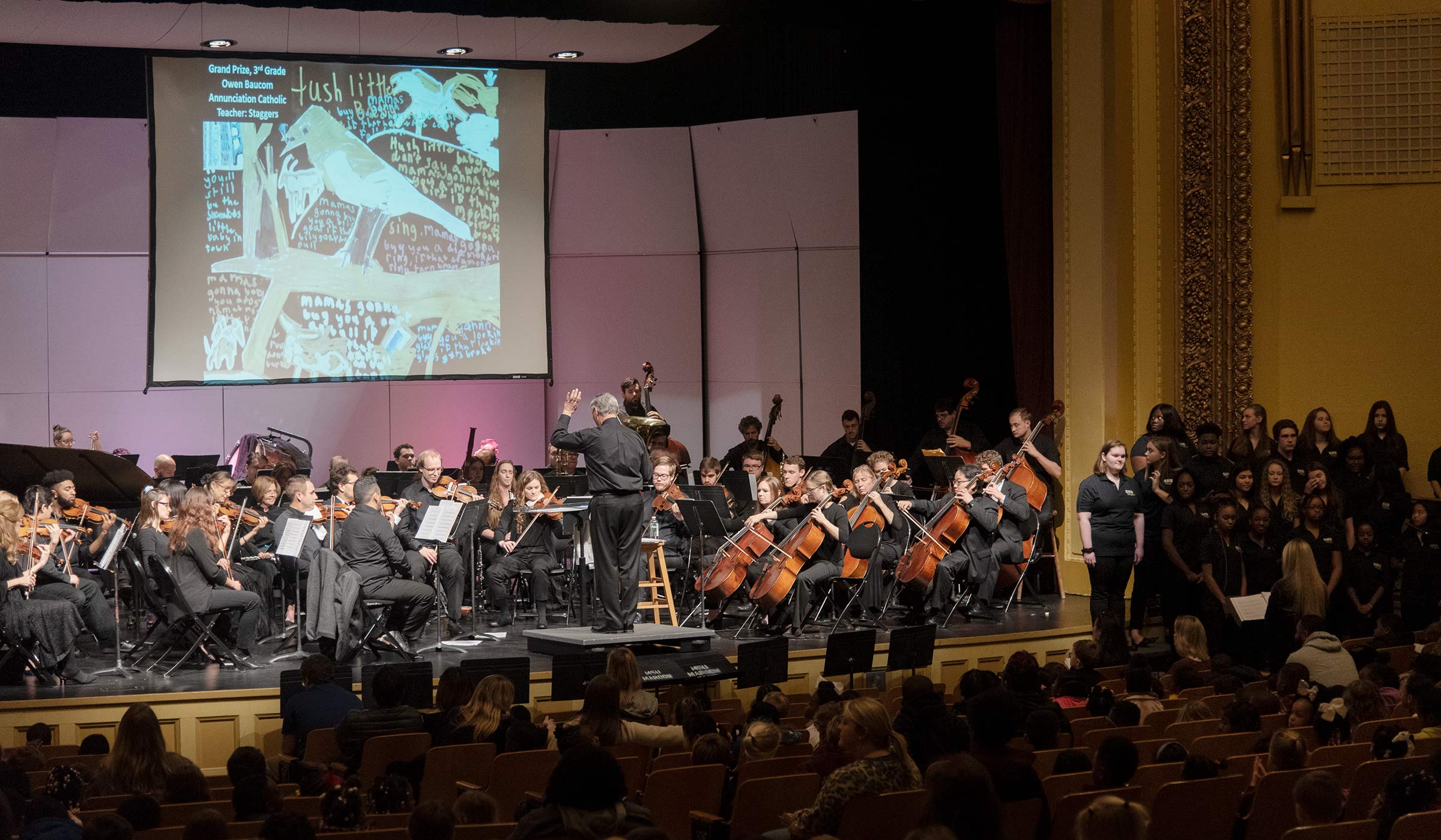 Symphony musicians dressed in all black with instruments on stage performing for audience