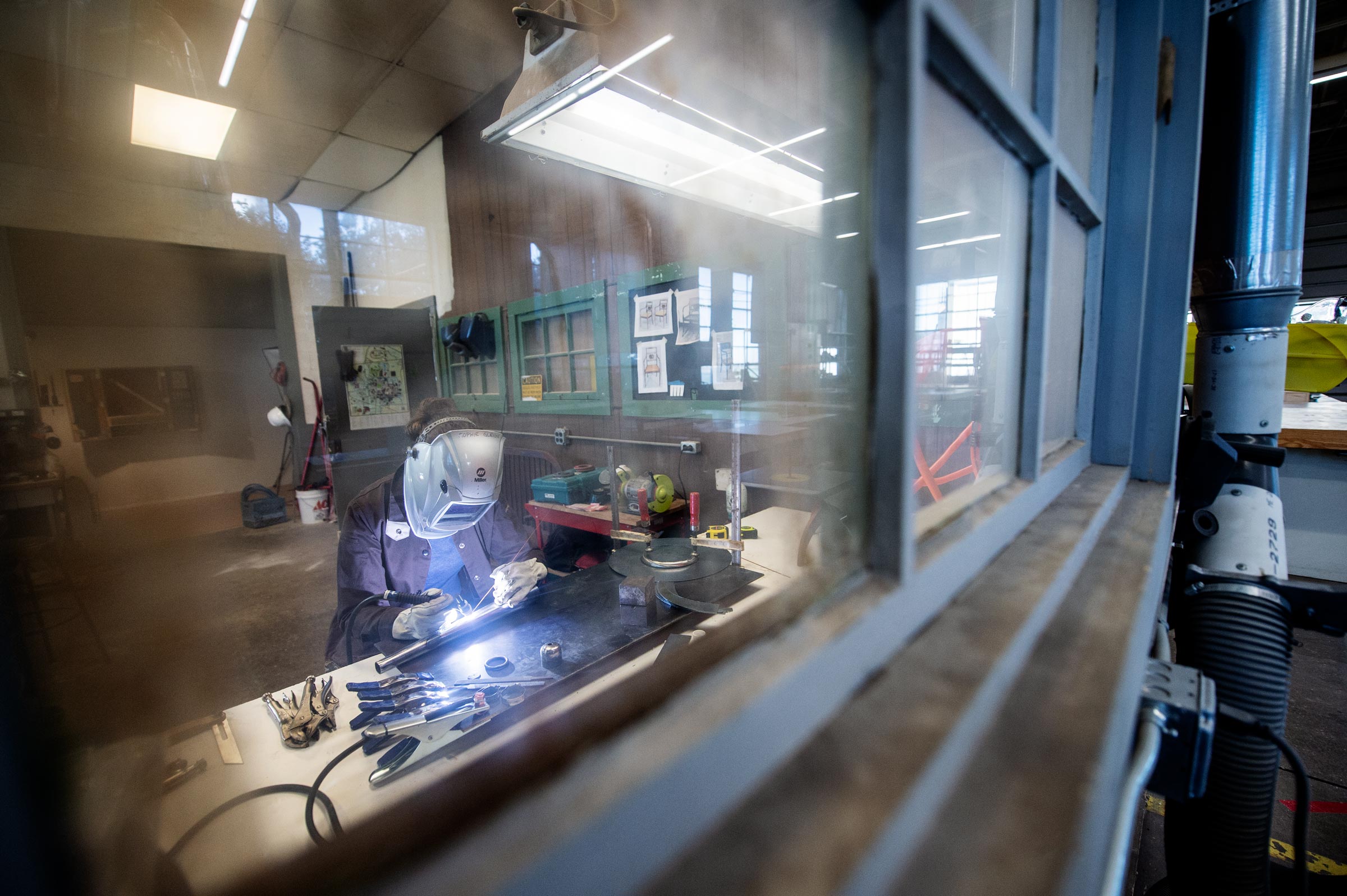 Viewed through panes of glass in the Sculpture Studio, Visiting Art Professor Sophie Glenn welds a table leg.