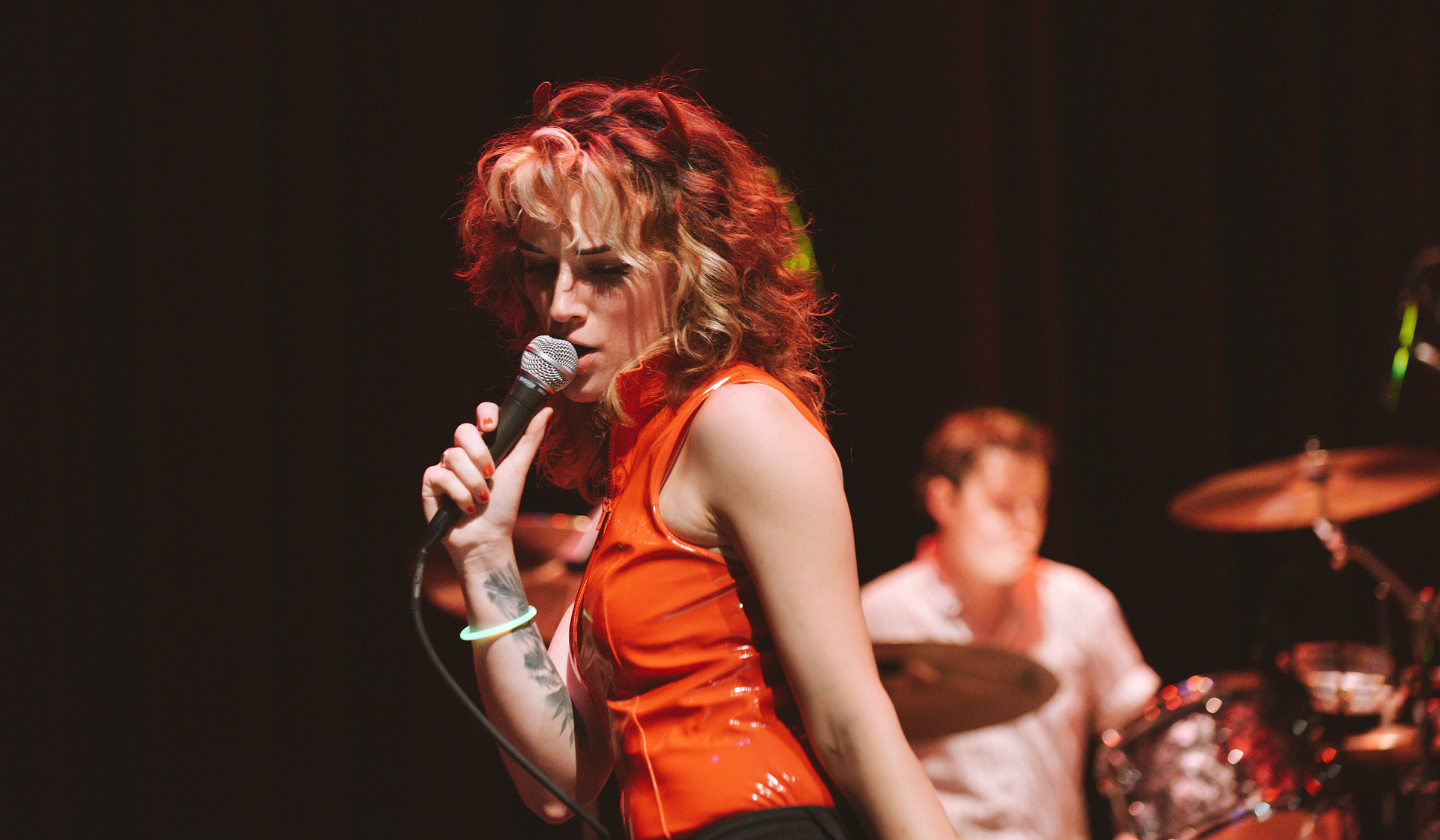 The lead singer of the rock band Flight Attendant sings into a mike on the Bettersworth stage, with band&#039;s drummer behind her.