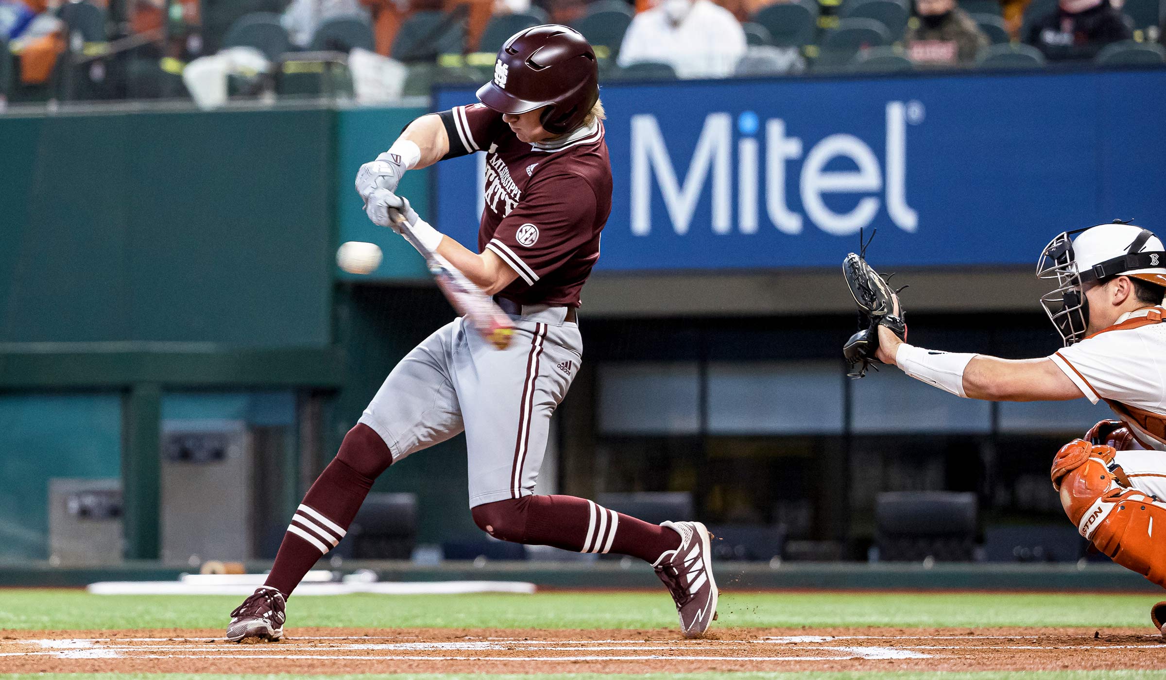 Baseball player in maroon and gray swinging at a baseball