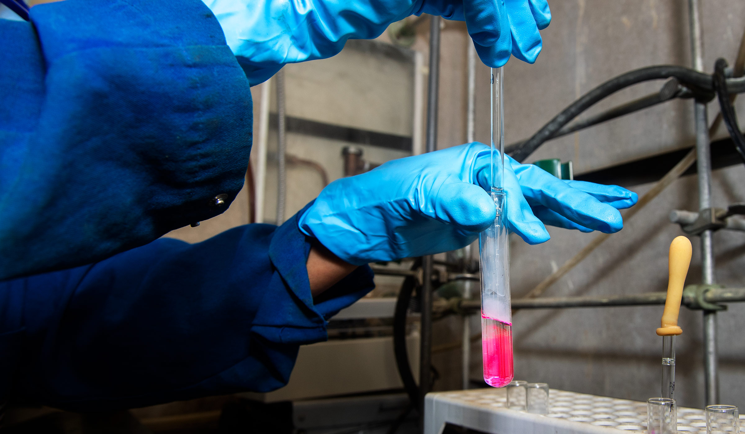 Gloved hands with dropper and vial of bright liquid