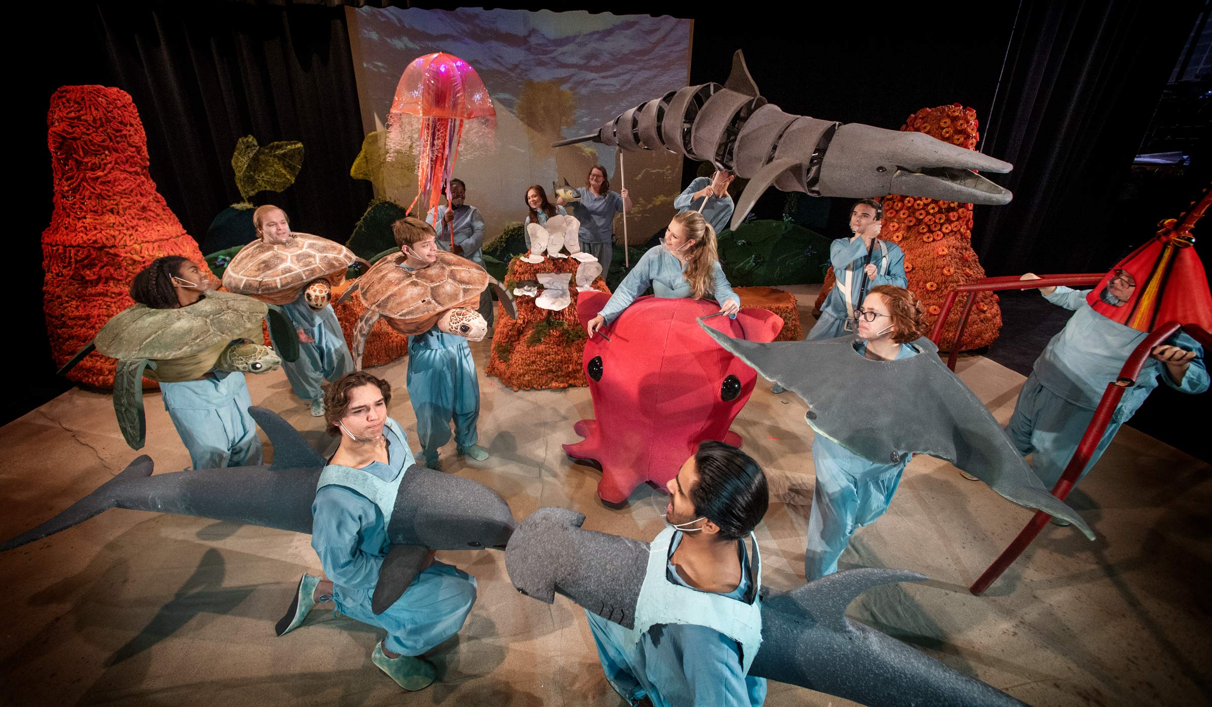 The cast of sea creature puppets pose on the McComas stage before a performance, including wearable puppet creatures such as turtles, a jellyfish, an octopus, and a bottlenose dolphin.