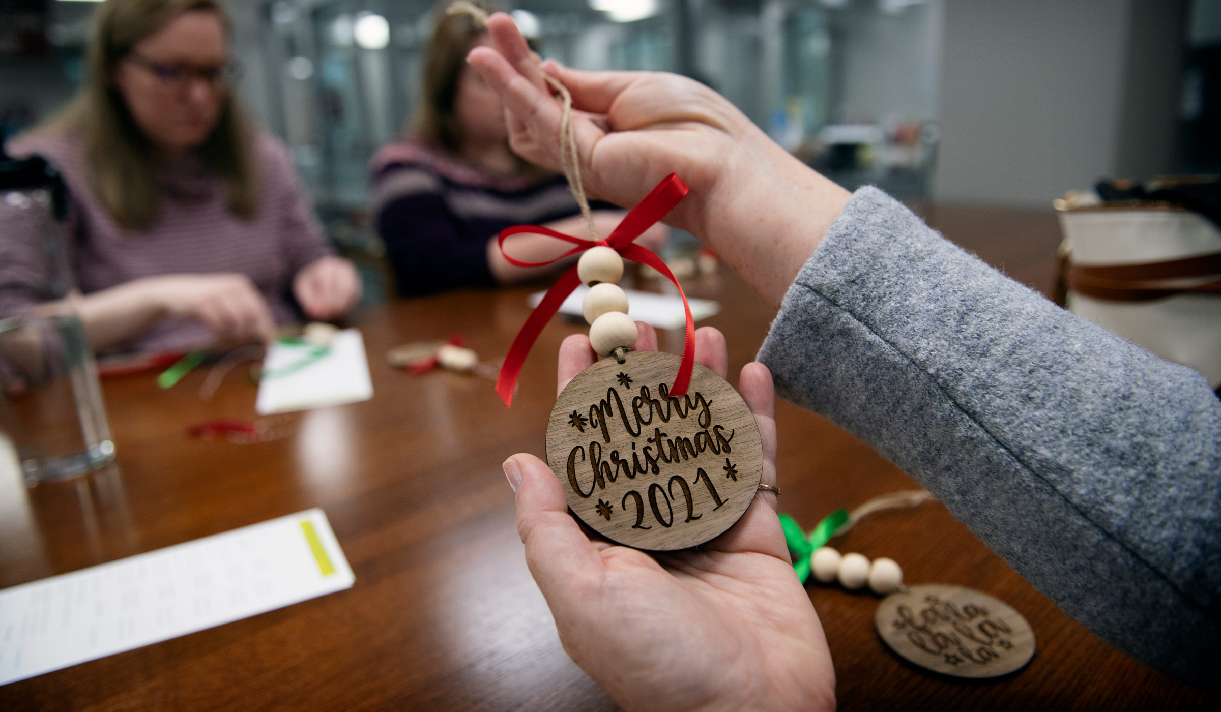 Hands hold a wooden ornament etched with &quot;Merry Christmas 2021&quot; Glowforge engraving at the Library&#039;s DMC Maker Space