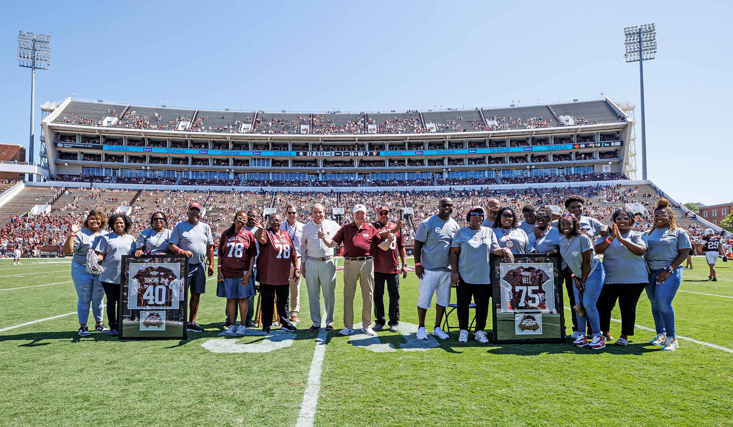 Group of people on football field smiling and waving with framed jerseys