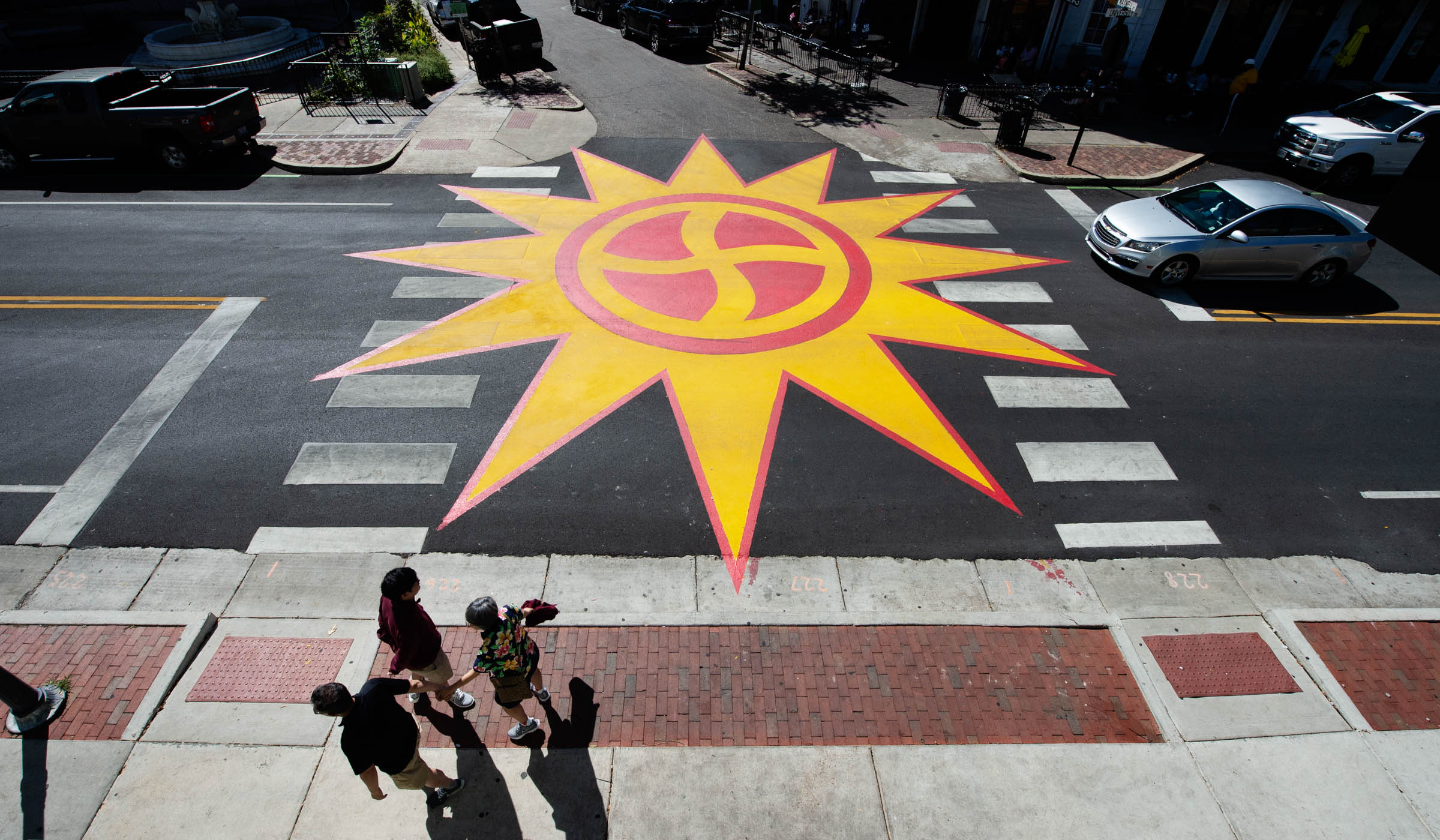 View looking down on a massive yellow and red sun symbol, which fills the Cotton District intersection of University Drive with Maxwell street.