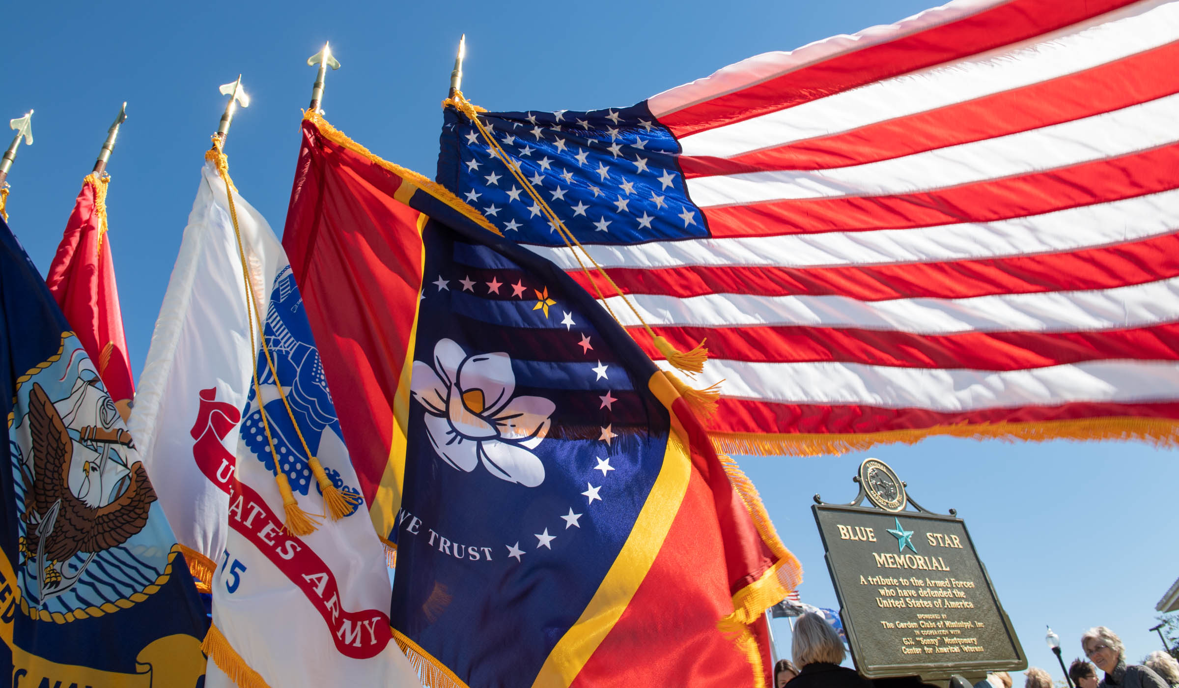 The freshly unveiled Blue Star Memorial is on the bottom right, framed by blowing flags of the US, MS, and Armed Forces.