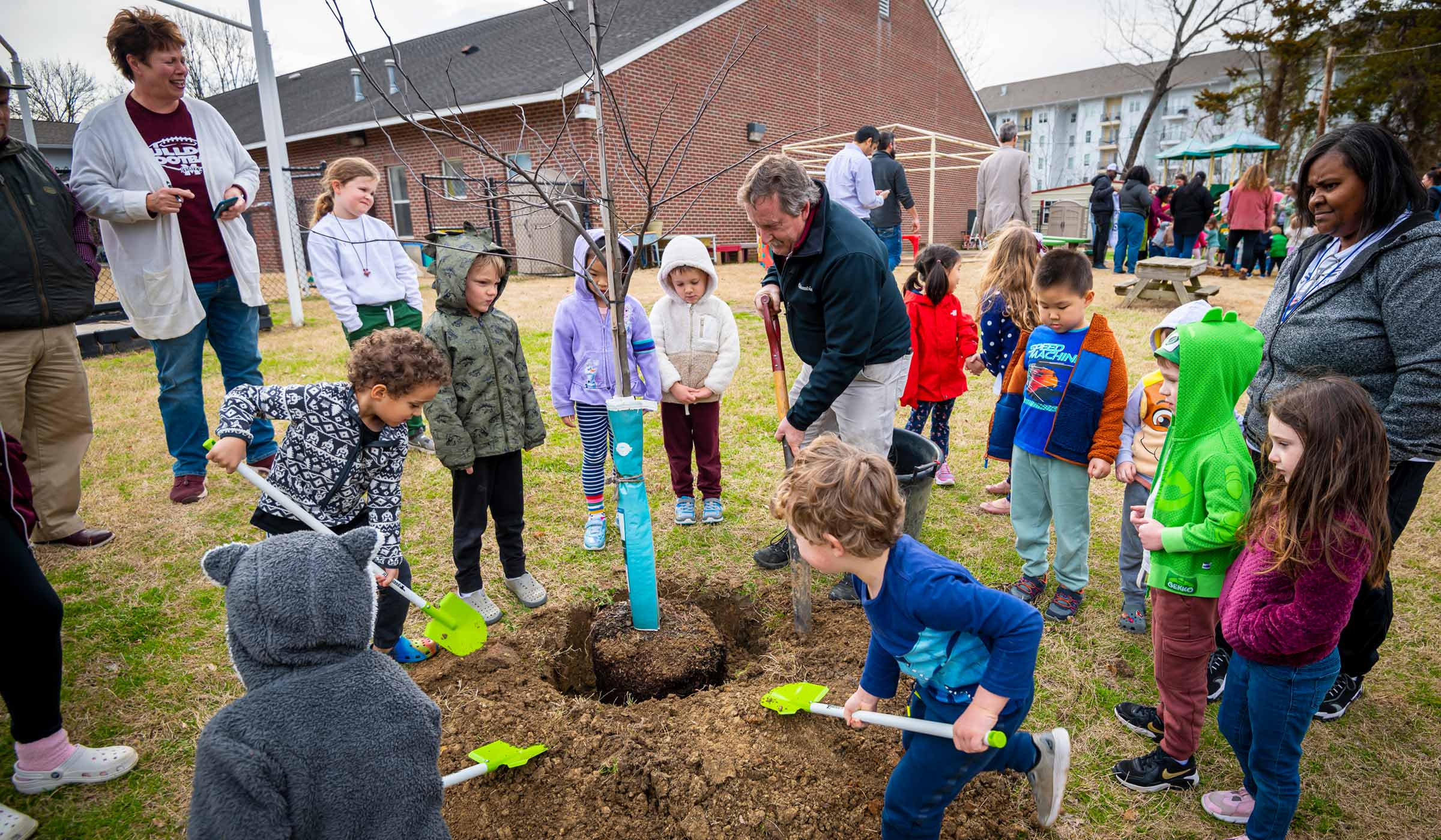 Kids helping to plant a tree with bright green shovels.