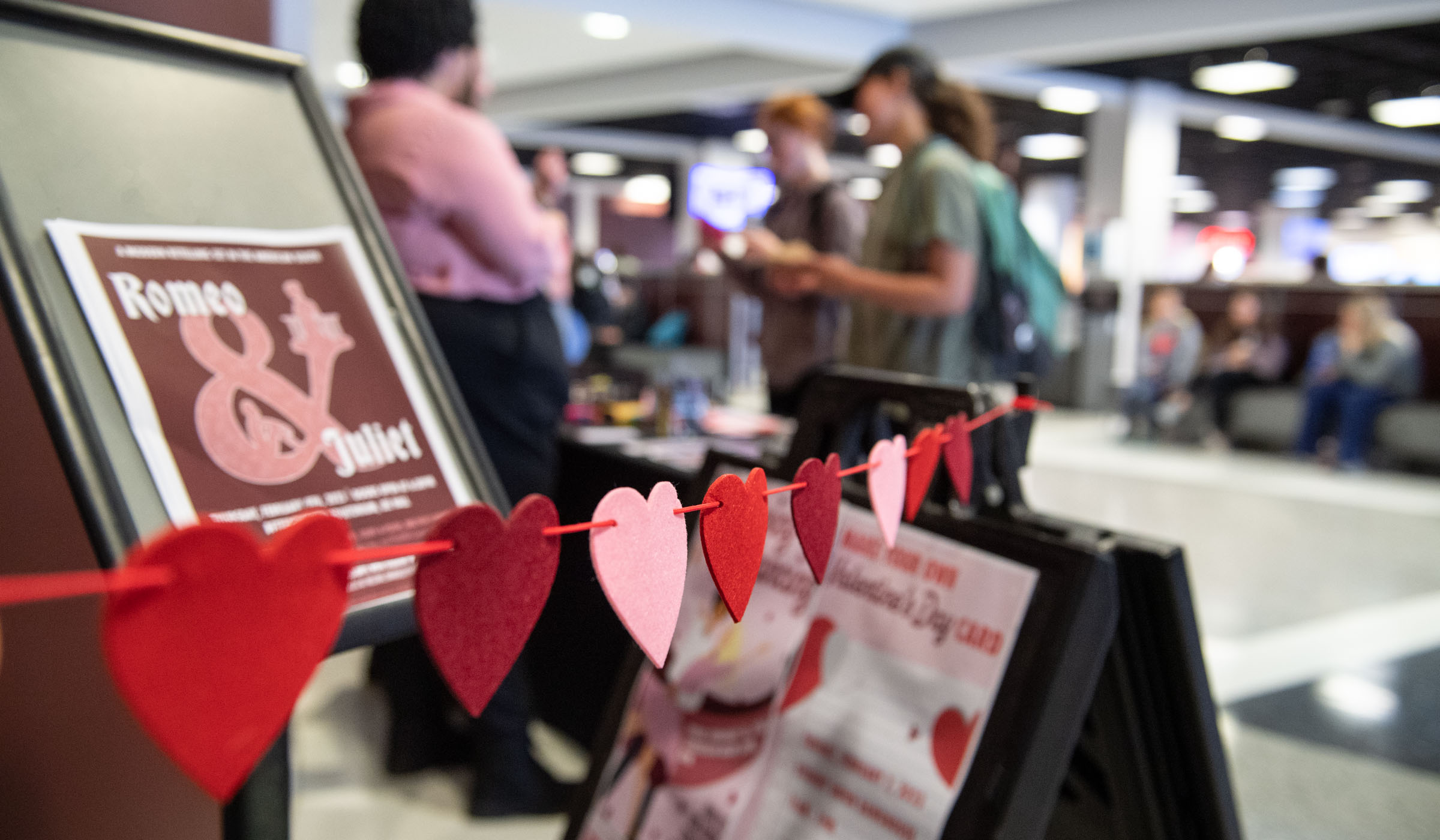 A garland of pink and red hearts demarcates a Student Activities outreach table in Colvard Union, promoting Romeo and Juliet and Dance Marathon events.