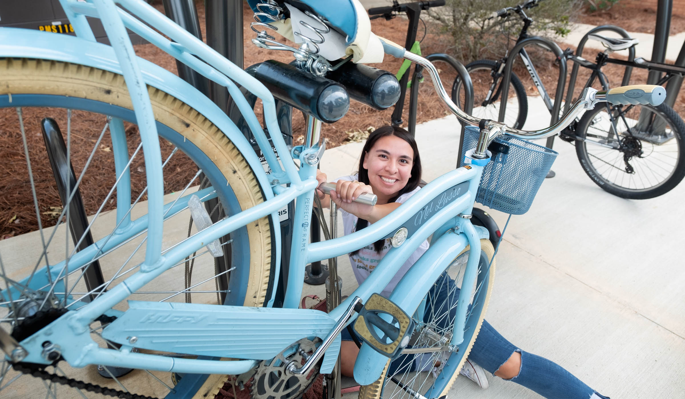 Looking up at the camera with her face framed by her blue bicycle, student Jayna Ben fills her bike tires at one of the covered bike stations near McCool Hall.