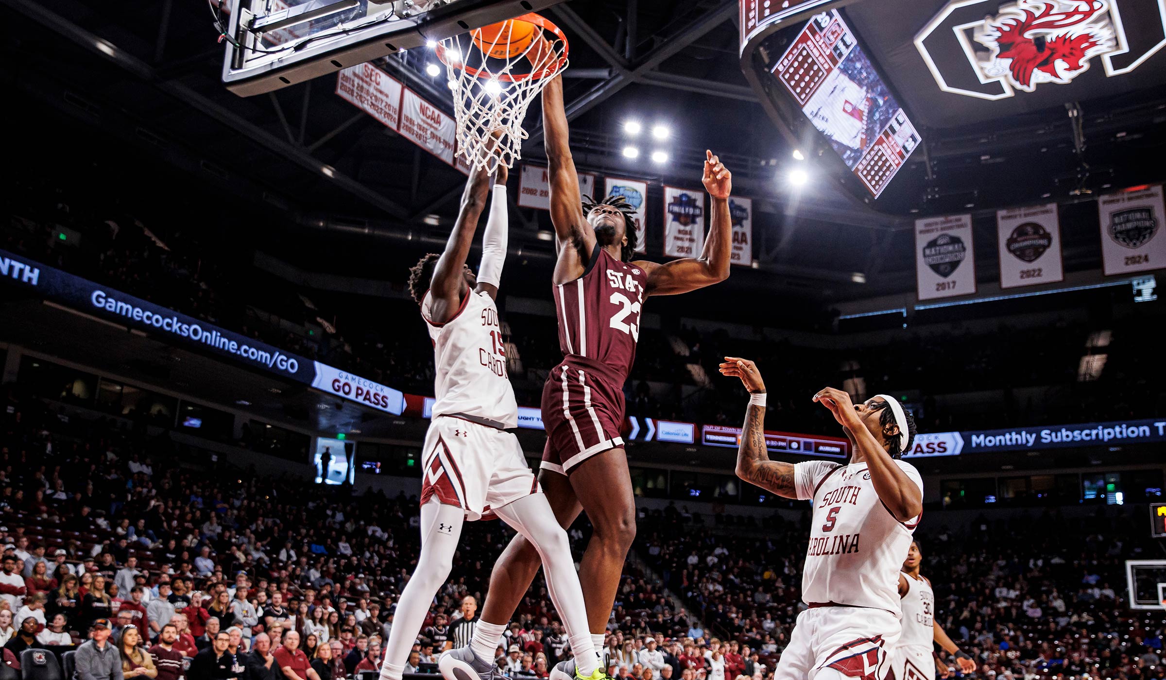 Man in maroon basketball uniform lifting ball into the basket over defenders