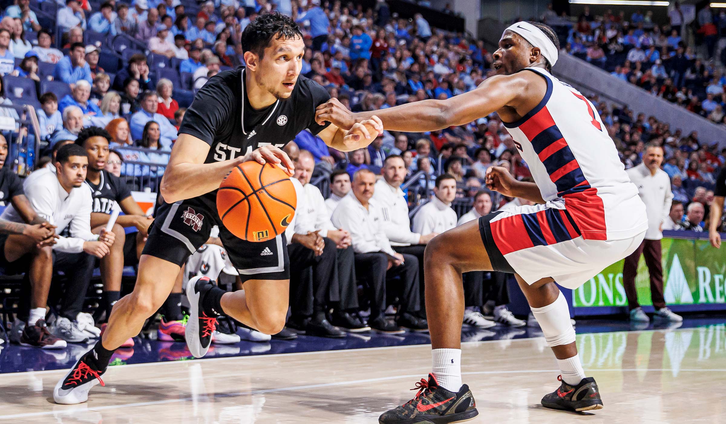 Basketball player in black driving towards basket versus player in all white 