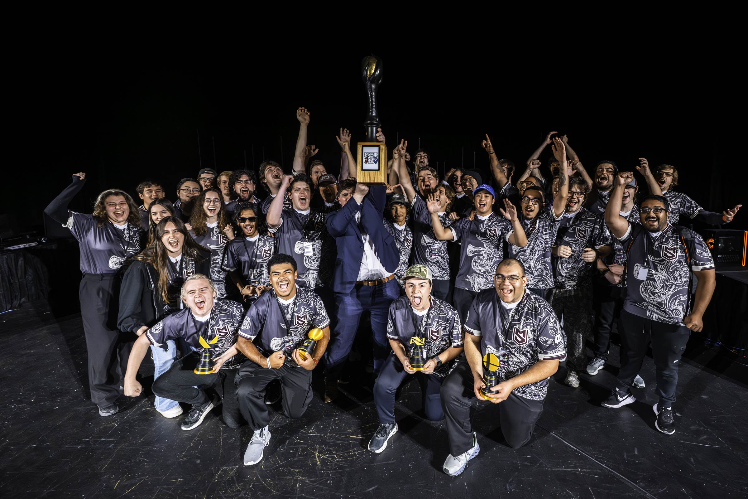 MSU Esports celebrates a 5-4 game victory over Ole Miss at the 8th annual Egg Bowl, proudly hoisting the golden egg trophy. The tournament, hosted in McComas theater, features live "best-of-seven" gameplay of popular competitive titles such as Rocket League, Marvel Rivals, Street Fighter Six, College Football '26, Valorant, League of Legends, and Super Smash Bros Ultimate. 