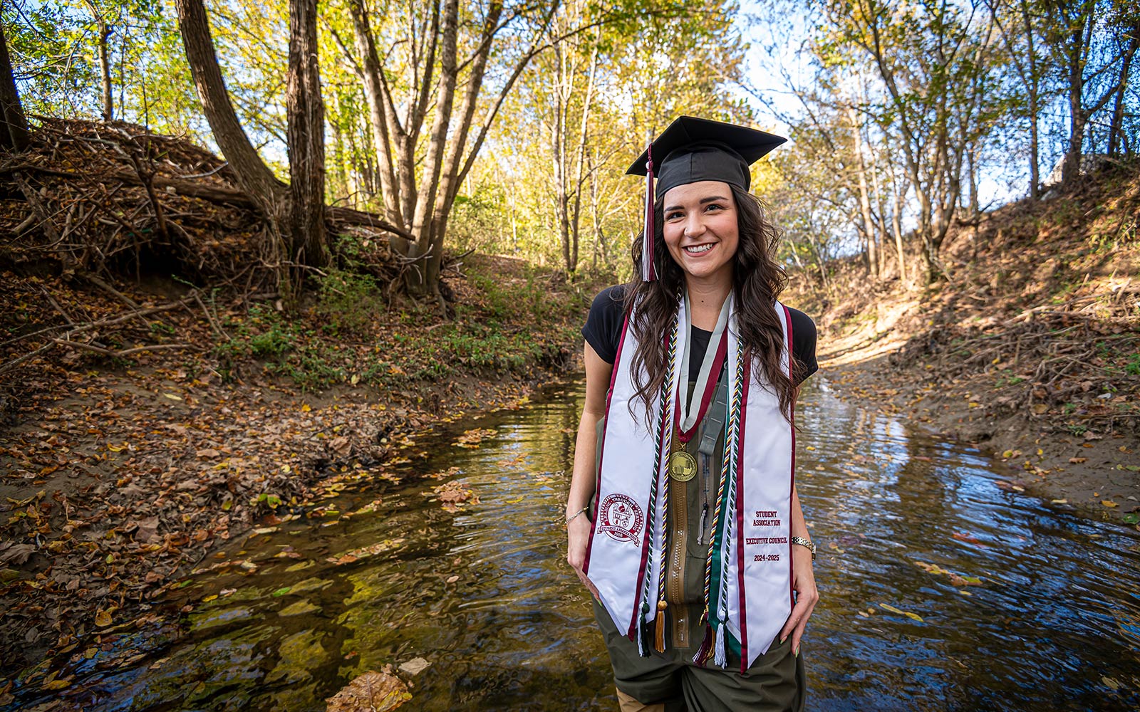 girl in graduation regalia in creek