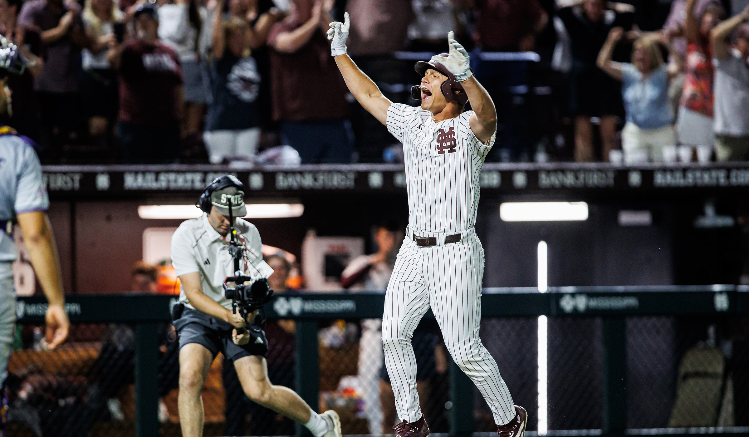 Baseball player in maroon and white pinstripe uniform jumping in the air while running bases in celebration.