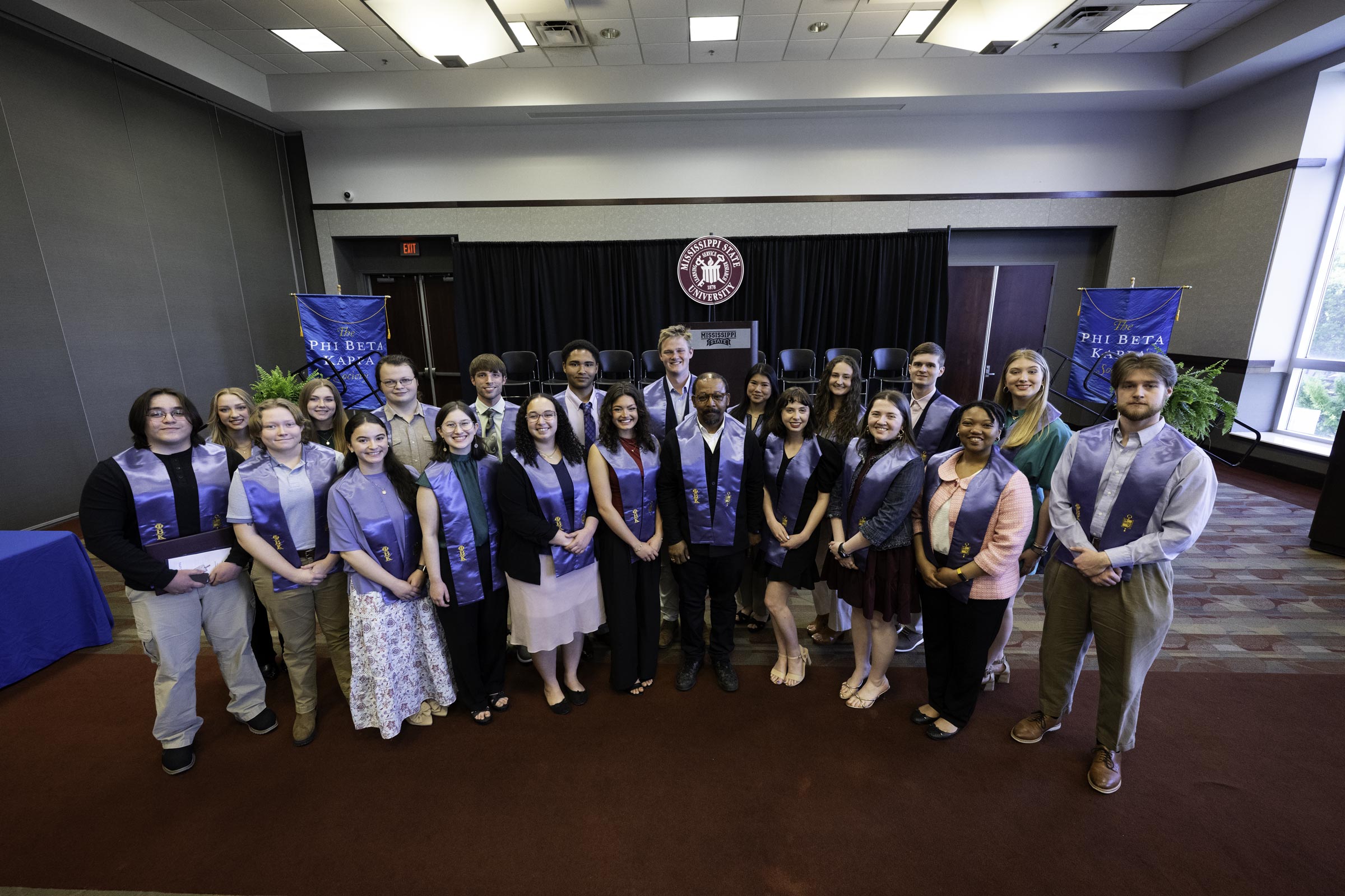 A large group of students wear royal blue stoles while smiling for a photo