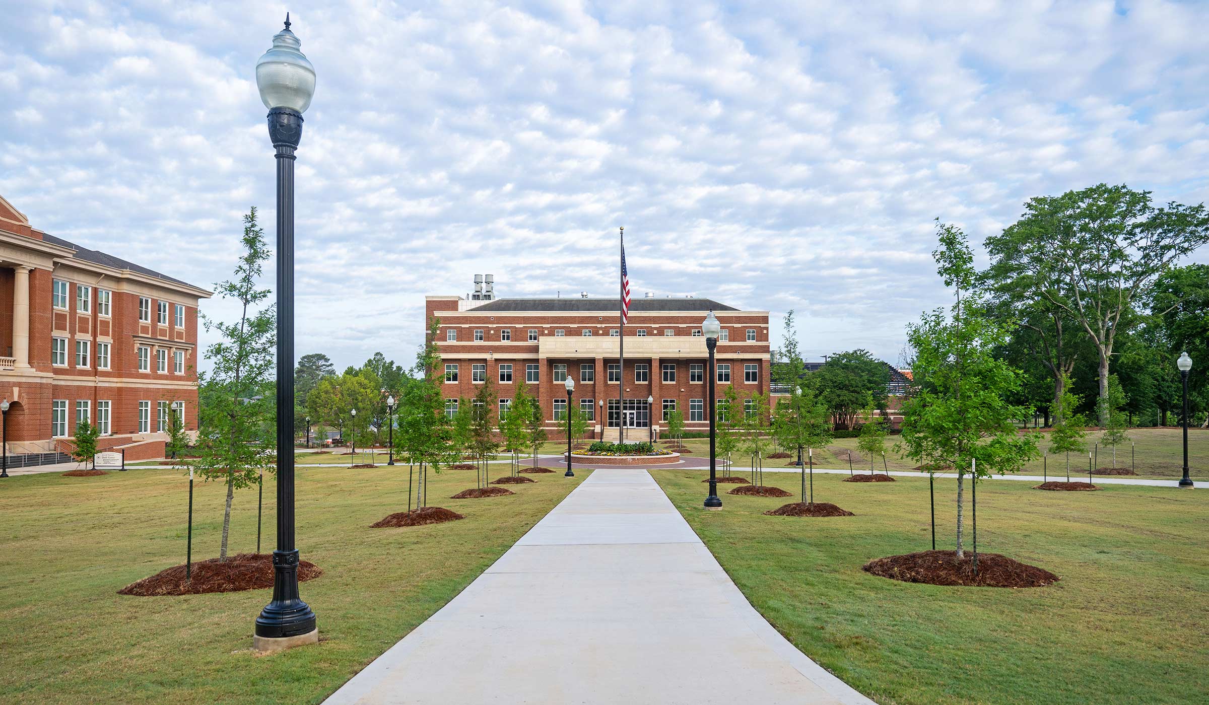 A sidewalk in McCarthy Quad, lined with trees, leads to a flagpole in the center of the quad.