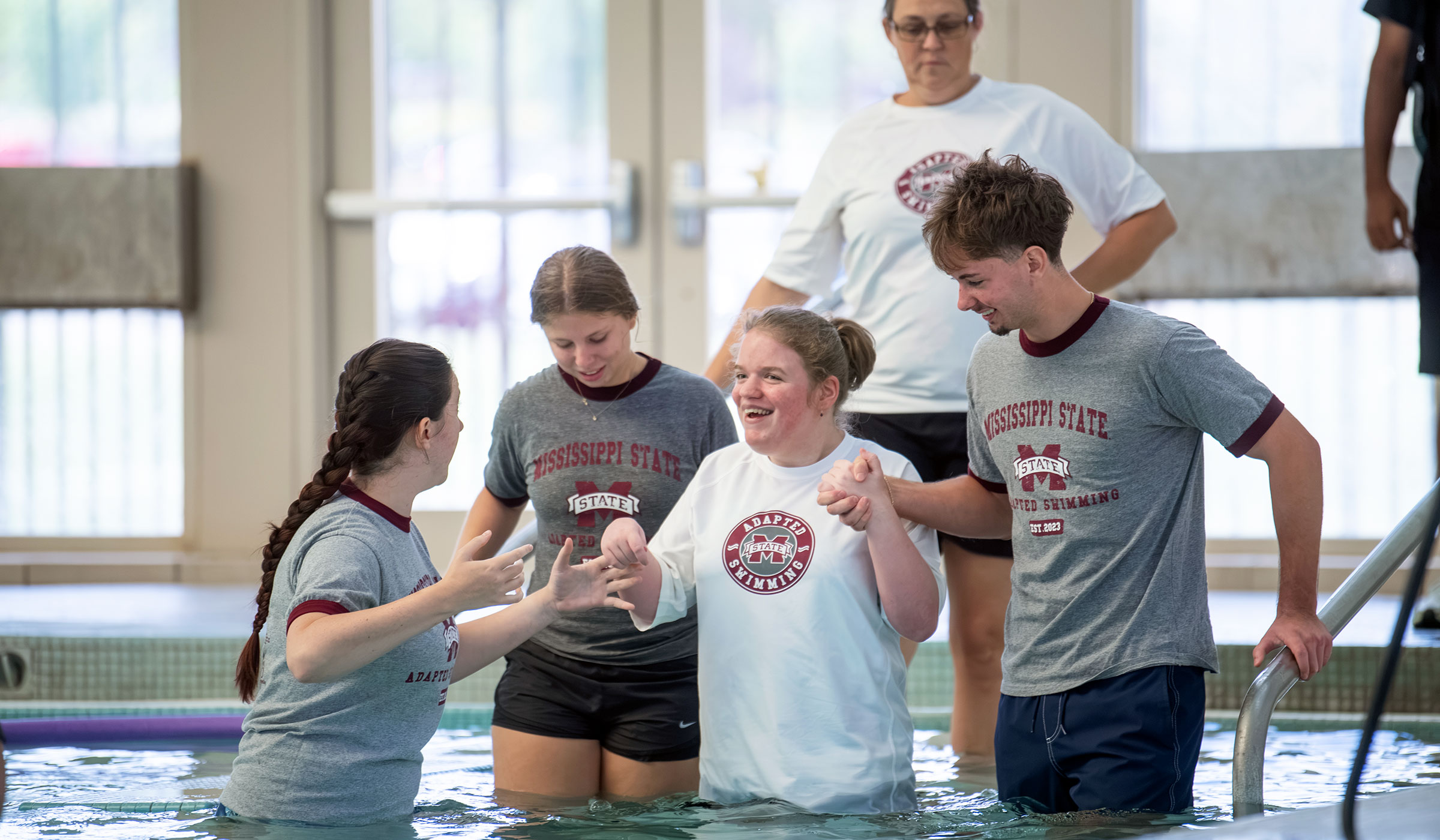 Mississippi State Adapted Swim volunteers help a camper into the Sanderson pool.