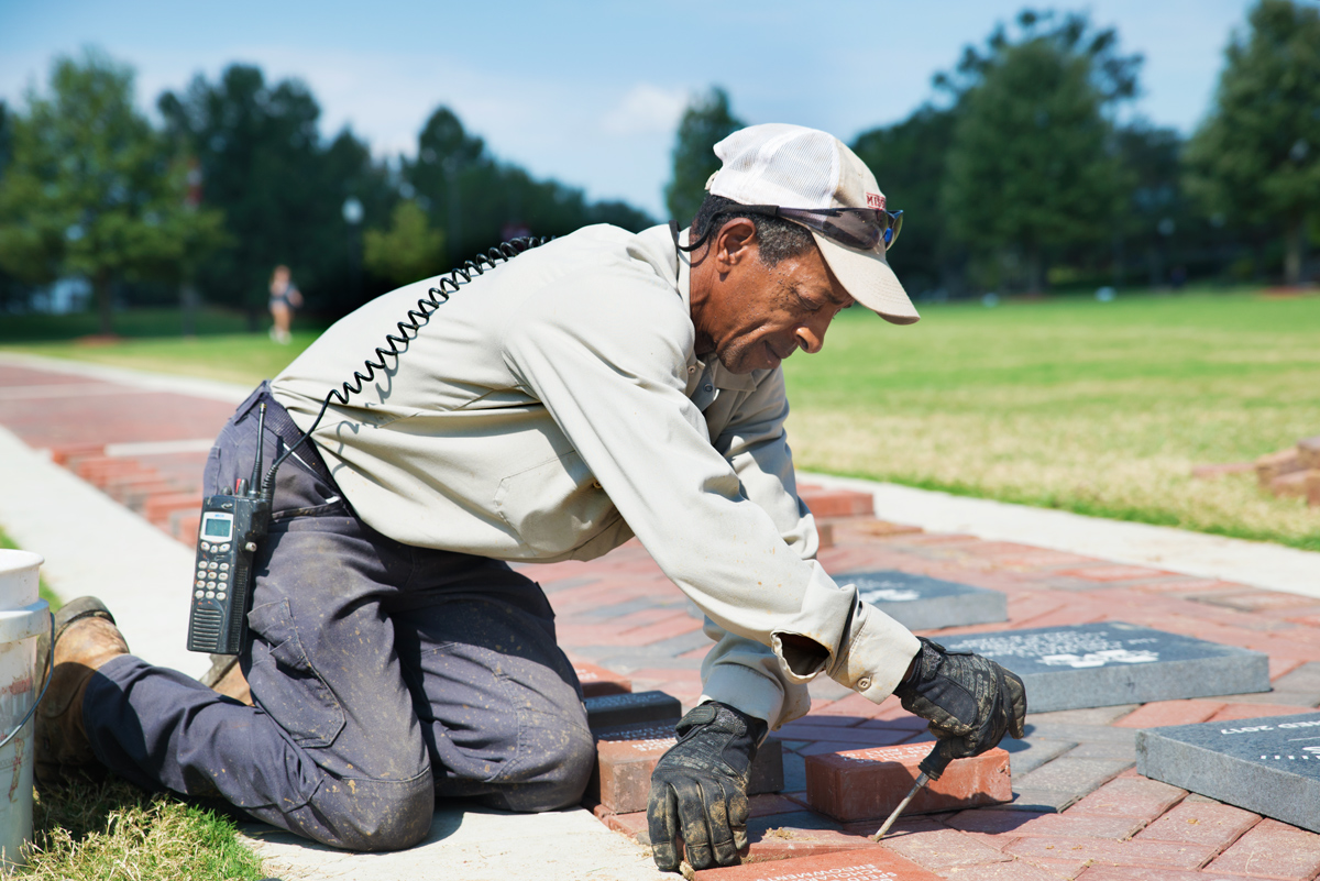 MSU Facilities employee Douglas Dumas kneels, laying donated bricks onto the Junction&amp;#039;s new Compass Scholars Walk.