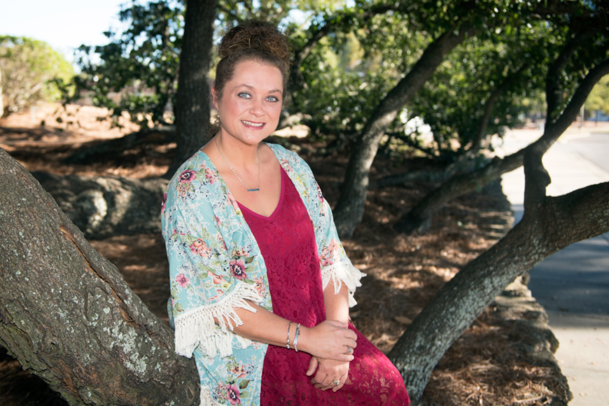 Portrait of Brandy Moss outside on the campus of MSU where she is seated on a low branch of a tree.