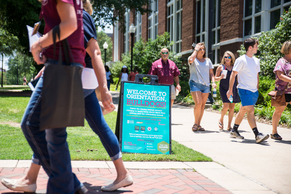 Incoming freshmen and their parents walk by an Orientation sign.