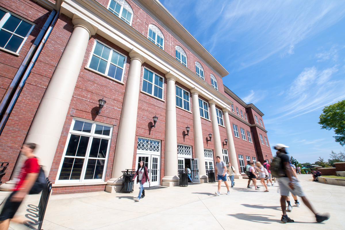 Students walking on sidewalk near red brick building with ivory faux columns