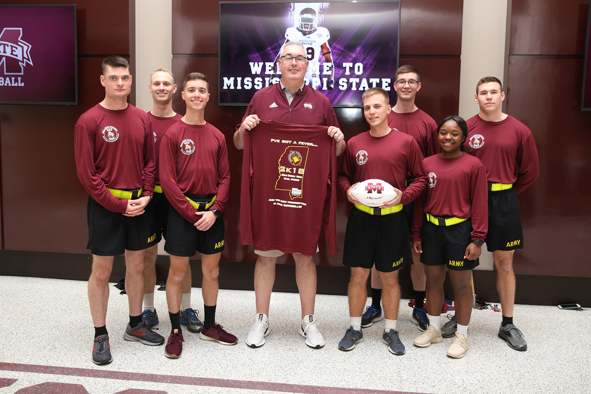 Army ROTC members in maroon running gear with Coach Joe Moorhead and signed football