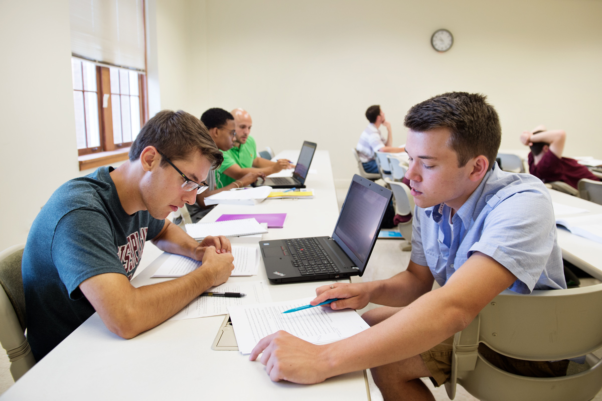 Two students discuss evaluate each other&amp;#039;s English composition drafts at the edge of a classroom.