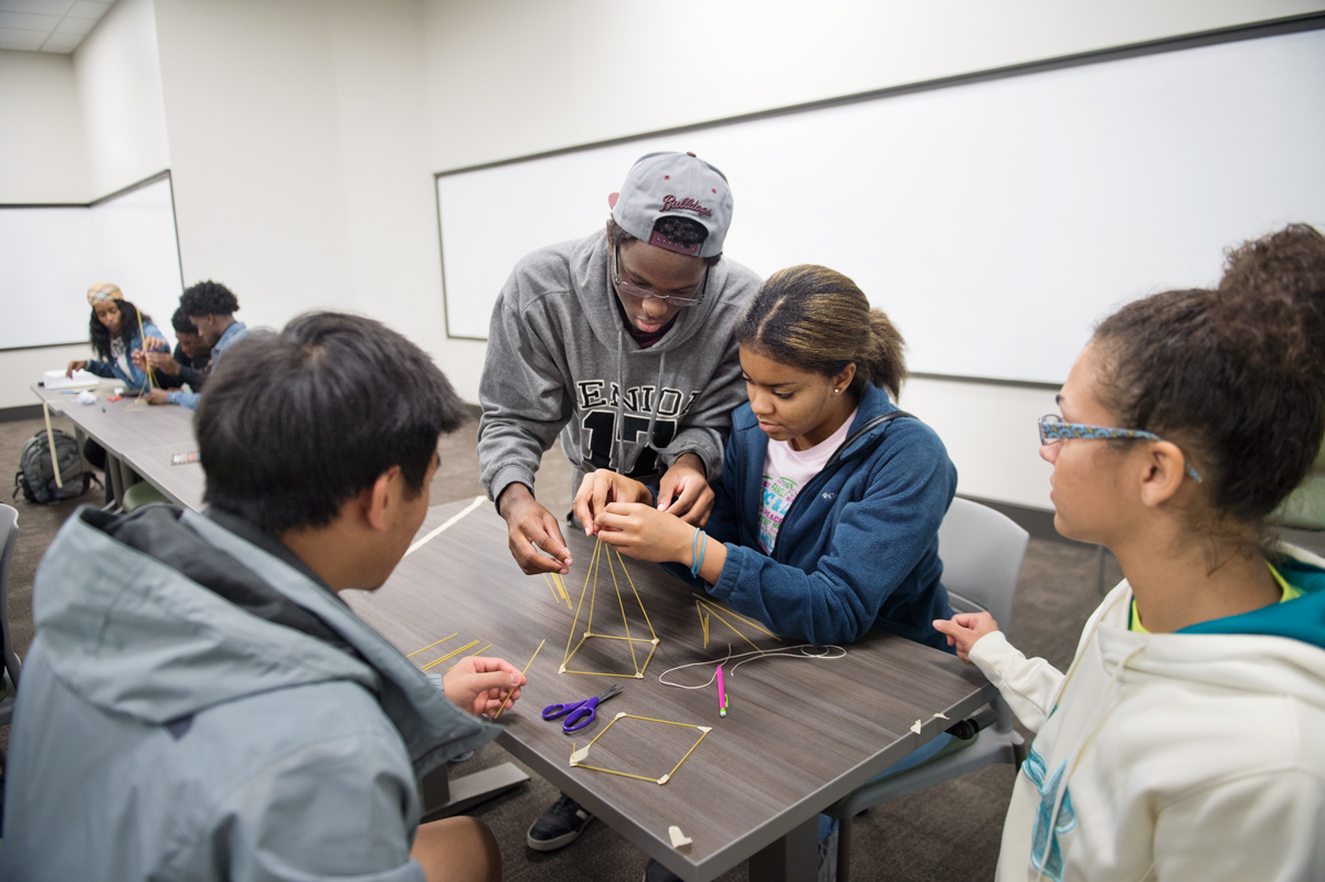 A team of four students work on building a structure made of spaghetti and tape as part of a collaborative exercise.