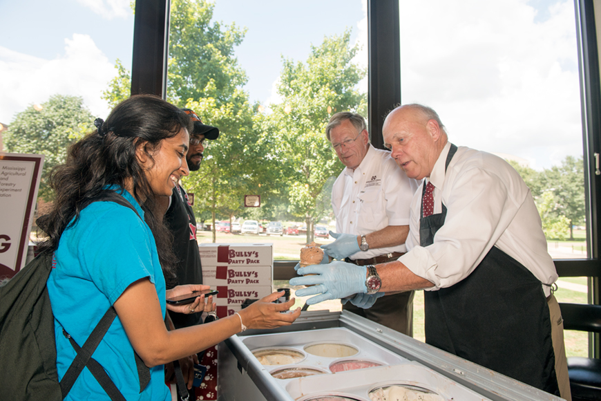 Student in blue shirt and backpack receives ice cream at the MAFES Sales Store from George Hopper.