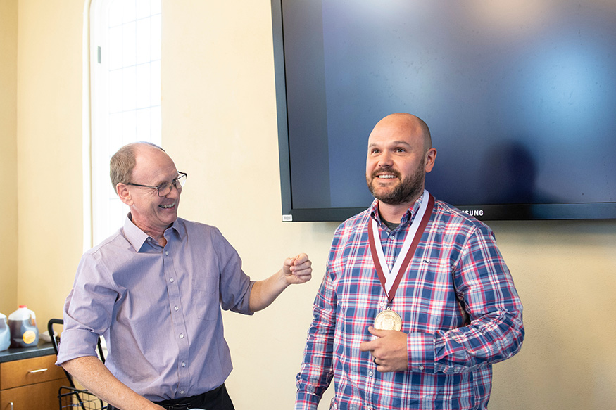 Man on the left smiles and man on the right wears new medallion