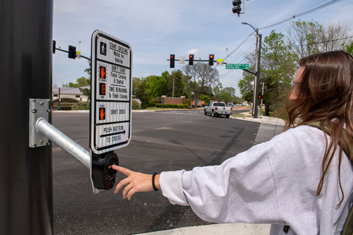 A student presses the "walk" button at the intersection of Bulldog Way and East Lee Boulevard