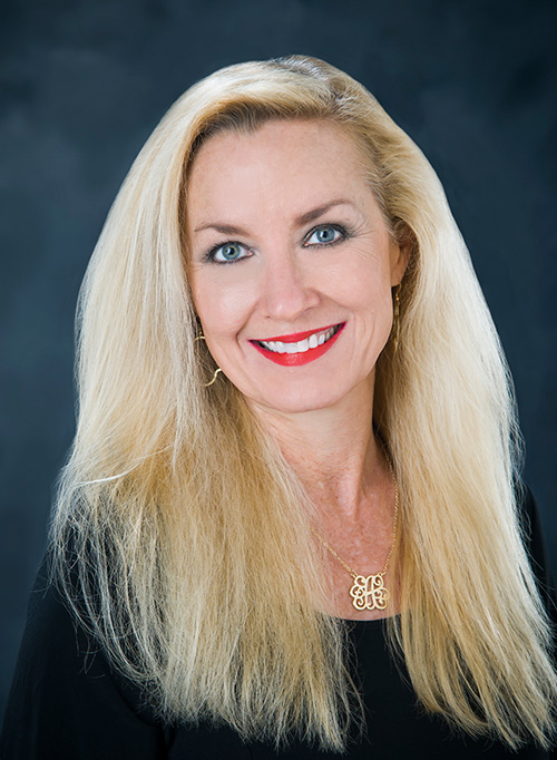 An up close portrait of Janet Carraway wearing a black shirt and gold monogram necklace