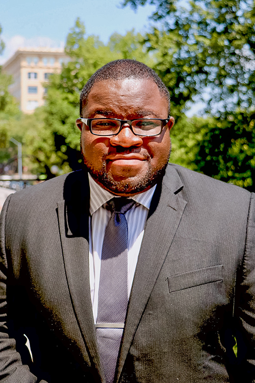 Dominique A. Quarles is pictured in a suit with trees and tall buildings in the background.