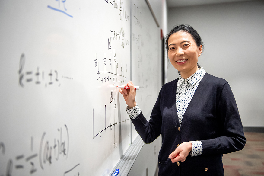 Jenny Du, pictured writing on a dry erase board in a classroom