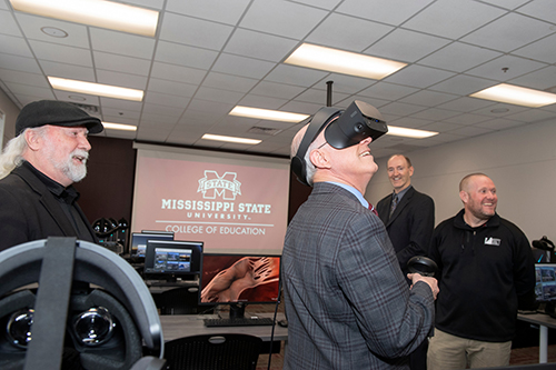 MSU Provost David Shaw smiles and looks around while wearing a virtual reality headset as three other men look on.