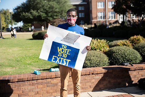 An MSU student holds a sign reading "To Vote is to Exist"