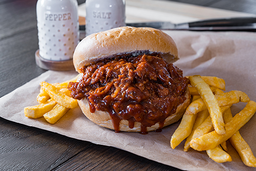 A barbecue sandwich is pictured surrounded by French fries on a plate. 