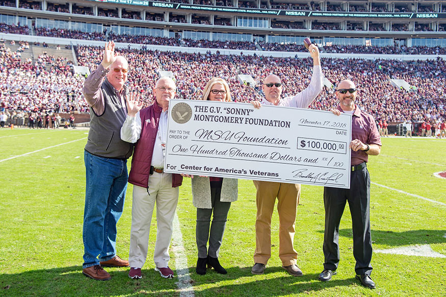 G.V. “Sonny” Montgomery Foundation board members presented a $100,000 gift in support of scholarships and services at MSU’s Montgomery Center for America’s Veterans. Pictured from left are board members Ronnie Walton, Kyle Steward, and Pam Stevenson, along with Brad Crawford, foundation president and executive director, presenting a ceremonial check to Brian Locke, director of the MSU center during MSU’s Nov. 17 home football game. (Photo by Beth Wynn)