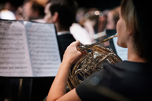 Musician plays a French horn during performance at MSU's McComas Hall