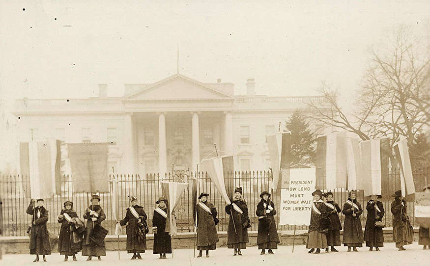 A vintage, sepia-toned photo shows members of the National Woman’s Party picketing in front of The White House
