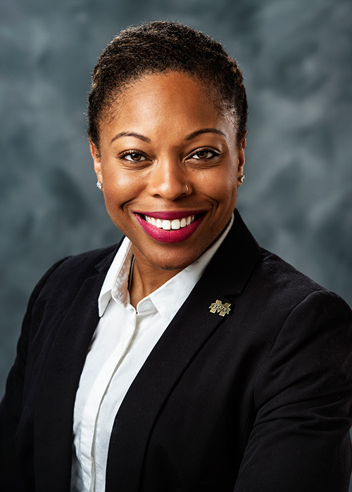 Studio portrait of Shandrea Stallworth wearing a business coat in front of a gray background