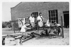 Early black and white photo of MSU students working on farm equipment.