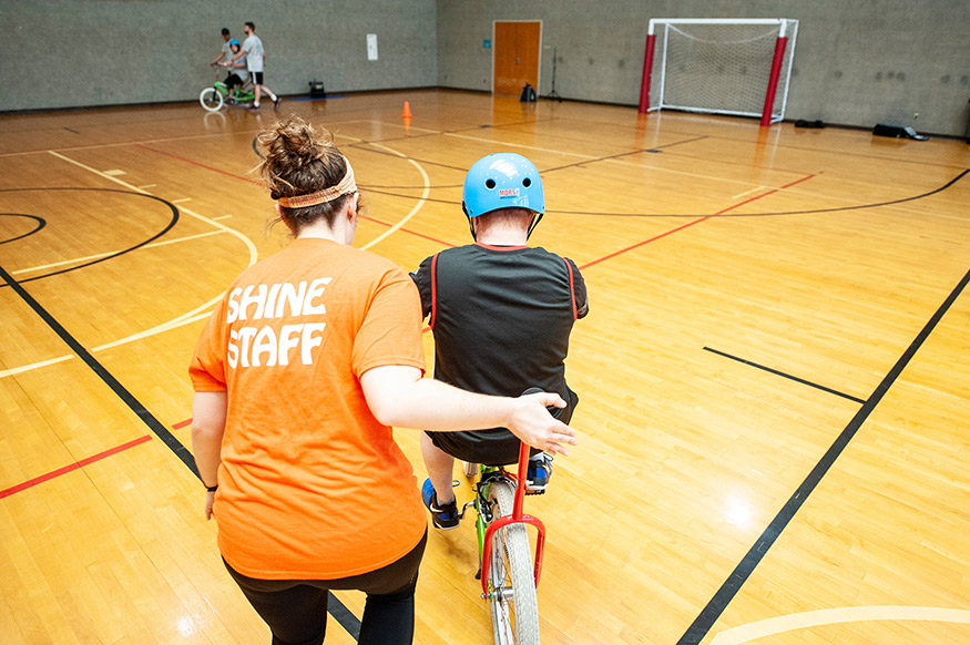 A camp staff member assists a youth learning to ride a bike