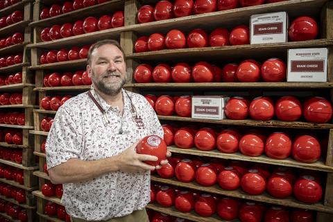 T.J. Evans holding a ball of cheese in front of a shelf full of cheese