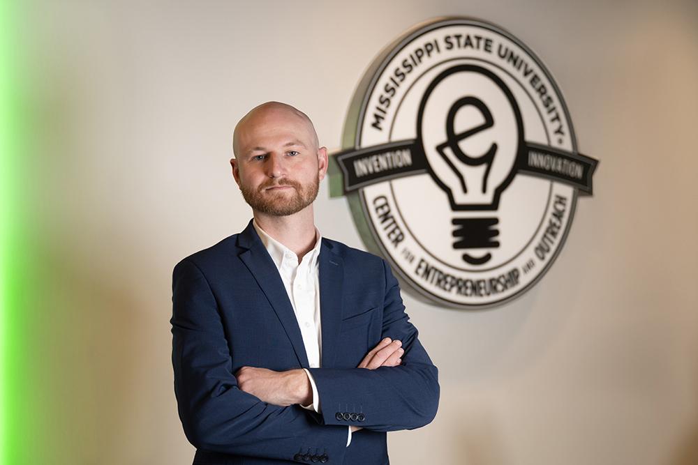 Nick Pashos poses in the McCool Hall E-Center, next to the center's wall-mounted logo.