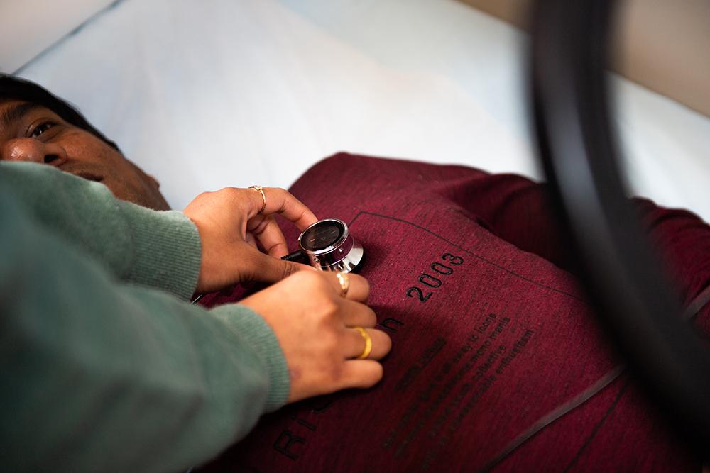 A student is pictured placing a stethoscope on a patient's chest.