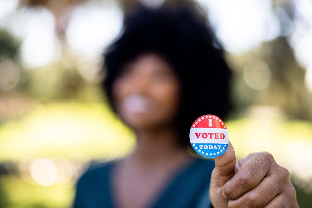 A person holds an "I voted" sticker with their thumb.