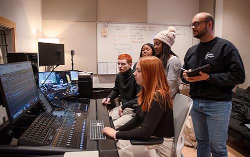 Students gather around a recording desk in a music studio.