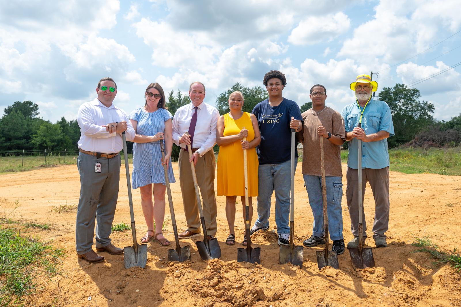 men and women stand on dirt pile with shovels